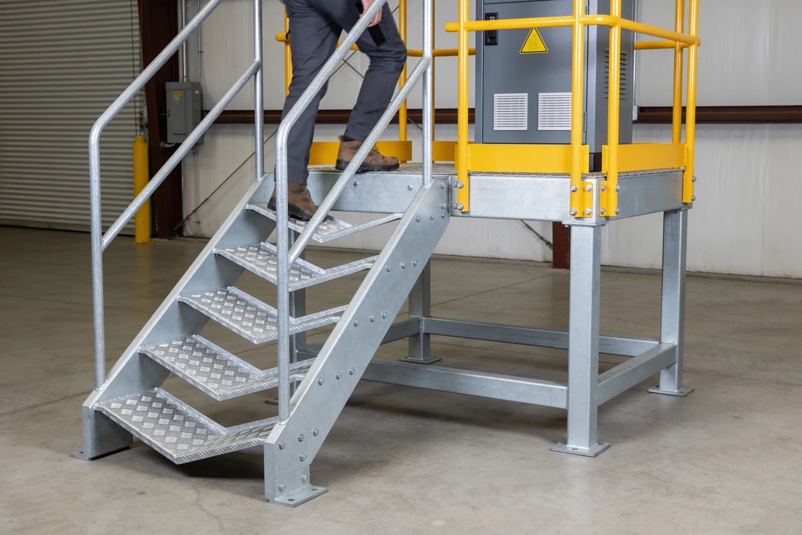 Small steel equipment platform with galvanized access steps and safety-yellow guardrails — the IBC 505.3 category where ladder access is permitted