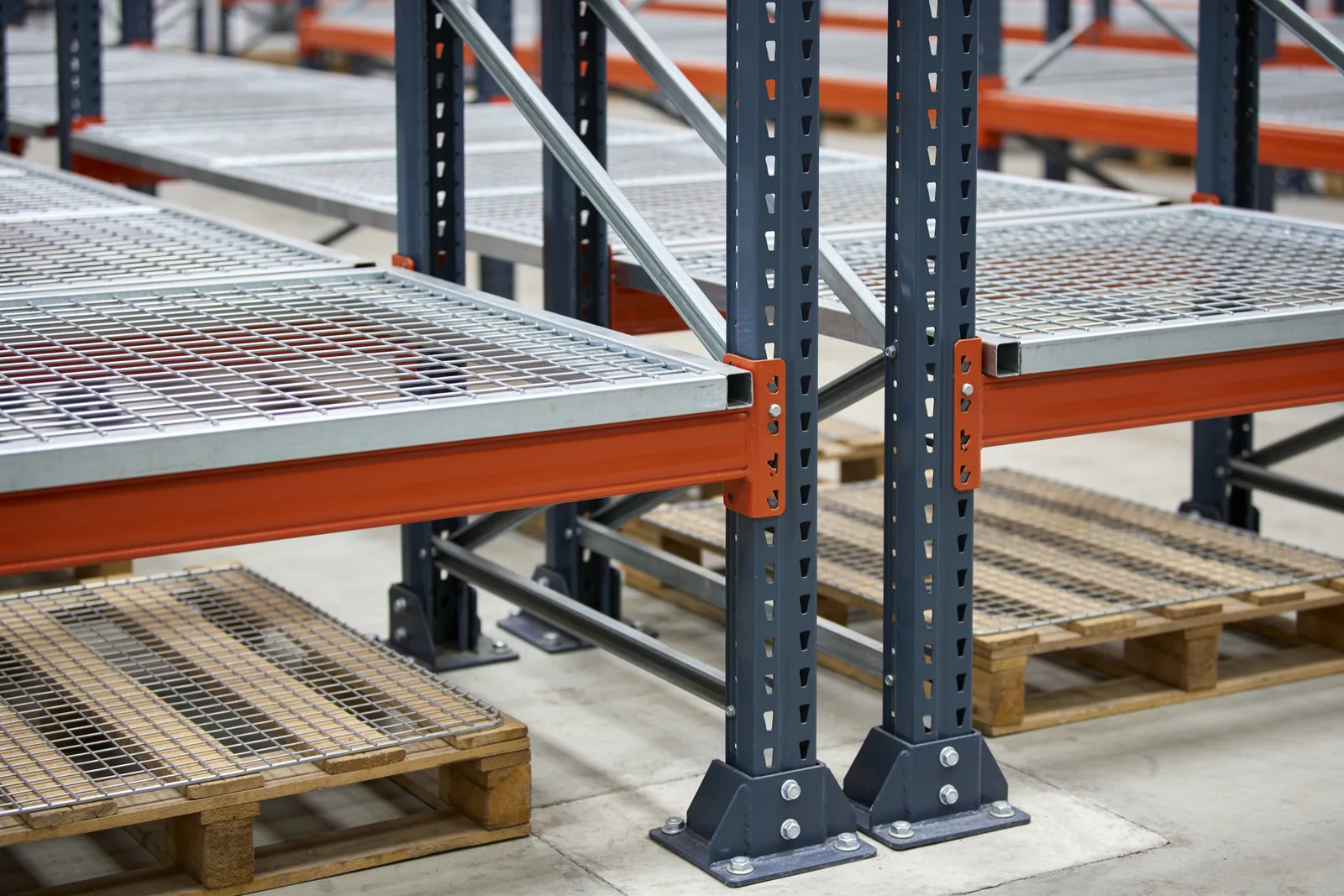 Close view of a rack-supported mezzanine connection: galvanized deck joists and bar grating bearing directly on teardrop pallet rack uprights with bolted base plates